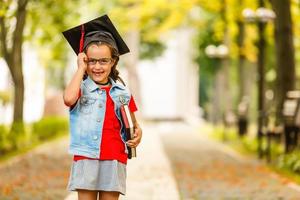 Authentic shot of cute little elegant girl with graduation hat is smiling during ceremony. photo