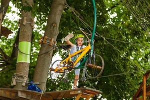 Little girl is standing on a rope, holding a rope with his hands. A child in a rope park passes obstacles photo