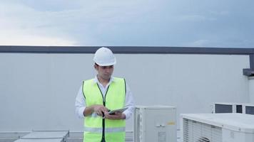 Asian maintenance engineer tablet recheck works on the roof of factory. contractor  inspect compressor system and plans installation of air condition systems in construction site of modern buildings. video