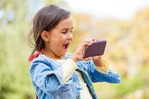 education, school, technology and internet concept - little student girl with smartphone in the park photo