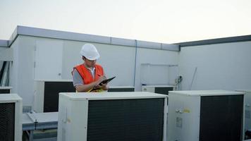 Asian maintenance engineer recheck works on the roof of factory. contractor  inspect compressor system and plans installation of air condition systems in construction site of modern buildings. video