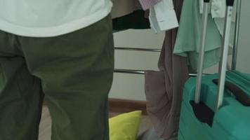 asiatische frau wählt kleidung für einen wochenendausflug. frauen packen taschen, um sich nach der staatlichen quarantäne auf die reise in den urlaub vorzubereiten. Frauen wählen unbenutzte Hemden aus, um sie zu spenden. video