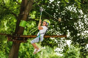 adorable niña disfrutando de su tiempo en el parque de aventuras de escalada en un cálido y soleado día de verano. actividades de verano para niños pequeños. niño divirtiéndose en vacaciones escolares. foto