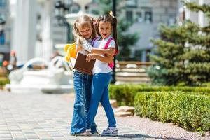 two school girls wearing backpack outside the primary school. schoolgirl, elementary school student going from school, graduation, summer holidays. photo