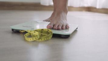 Woman foot stepping on weigh scales with tape measure. A woman is weighing herself after eating food. Woman serious about weight because need diet. Diet Concept and loss weight. video