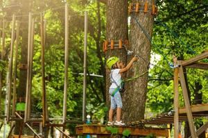 Portrait of little smiling girl in helmet and harness on trail in sky rope park in summer. photo