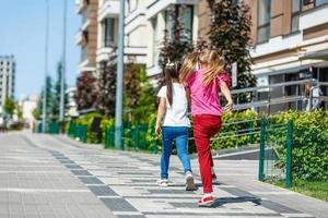 two school girls wearing backpack outside the primary school. schoolgirl, elementary school student going from school, graduation, summer holidays. photo