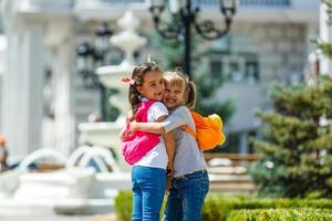 two school girls wearing backpack outside the primary school. schoolgirl, elementary school student going from school, graduation, summer holidays. photo