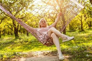 Smiling blonde woman relaxing on the hammock in garden, leisure time and summer holiday concept photo