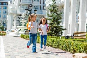 two school girls wearing backpack outside the primary school. schoolgirl, elementary school student going from school, graduation, summer holidays. photo