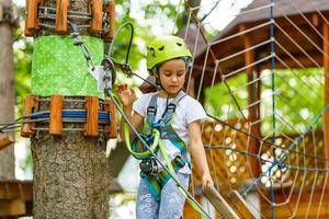 Adorable little girl enjoying her time in climbing adventure park on warm and sunny summer day photo