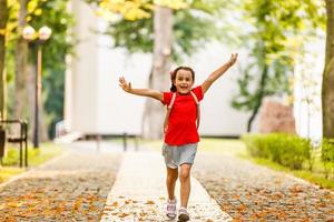 The little schoolgirl is running with a backpack and laughing. The concept of school, study, education, friendship, childhood. photo