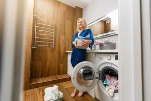 Beautiful young woman is smiling while doing laundry at home. photo