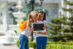 Two little happy cute girls playing on a tablet PC computing device at school. Education and self learning wireless technology concept. People lifestyles and friendship. Preschool children photo