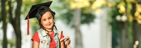 Happy school kid graduate in graduation cap looking up photo