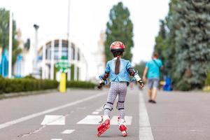 niña bonita y graciosa en patines con casco montando en un parque. concepto de estilo de vida saludable. foto