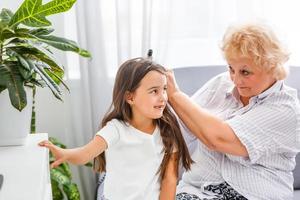 adorable niña juguetona con una niñera feliz de mediana edad en casa. linda nieta preescolar pequeña con abuela anciana emocionada. foto