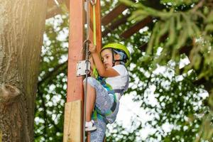 Niña de la escuela feliz disfrutando de la actividad en un parque de aventura de escalada en un día de verano foto