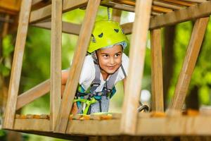 Happy school girl enjoying activity in a climbing adventure park on a summer day photo