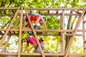 parque de cuerdas de escalada de aventura - niños en el parque de cuerdas del curso en casco de montaña y equipo de seguridad foto