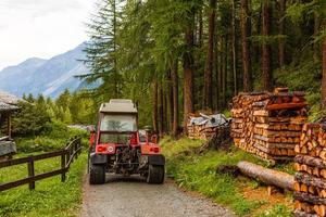 Homemade improvised tractor trailer made of strong metal stacked with prepared firewood and covered with tarpaulin for protection left in family house backyard surrounded with uncut grass. photo