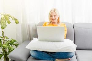 una joven feliz se relaja en un cómodo sofá y usa una laptop en casa. foto tonificada.