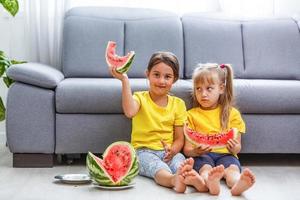 Child eating watermelon, two little girls eat watermelon at home photo