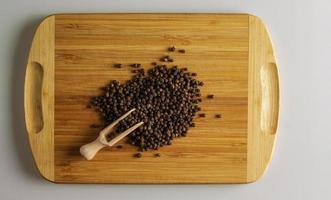 granos de pimienta negra. especia aromática para la comida. fondo de semillas secas de pimienta negra en una tabla de cocina de madera con una cuchara dosificadora. foto