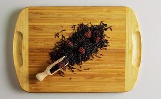 Background of dry tea based on black with whole raspberries on a wooden background. photo