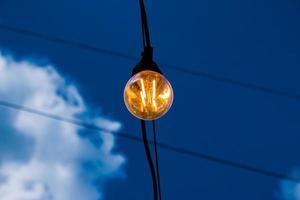 primer plano de un filamento de estilo edison en una bombilla de luz contra un cielo nublado. crisis de energía. foto