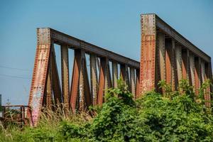 Old rusty bridge over the river. Transportation. Old metal railway bridge. Steel bridge across the river against blue sky. photo