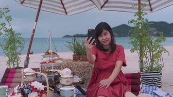 Beautiful Asian woman taking pictures of herself while traveling at sea. A woman is having a VDO conference with her family about food attractions by the sea. concept of relaxation video