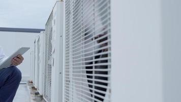 un ingénieur de maintenance asiatique porte un casque travaille sur le toit de l'usine. le superviseur inspecte le système de compresseur et planifie l'installation de systèmes de climatisation sur le chantier de construction de bâtiments modernes.