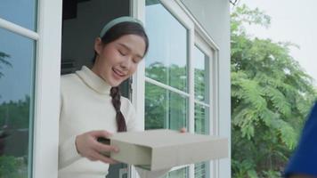 mulher asiática sorridente feliz recebe caixa de comida do correio na casa da frente. entregador de uniforme vermelho entrega expresso. compras online, recipientes de papel, takeaway, carteiro, serviço de entrega video