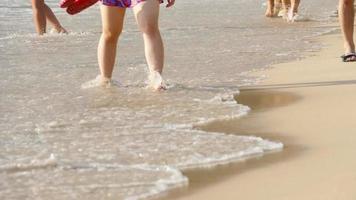 pessoas indo na areia lavada pelas ondas do mar. close-up de pé descalço andando na praia por trás. dia ensolarado de verão à beira-mar. video