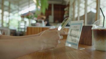 vrouw gebruik smartphone naar scannen qr code in cafe. de restaurant gebouwd een digitaal betaling systeem zonder contant geld. qr code betalen, e portemonnee, contant geld technologie, betalen online video