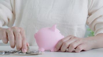 closeup of business woman hand putting money coin into piggy bank for saving money. wealth, Finance, business, investment, retirement, future, accounting, plan life, economize, conserve, family. video