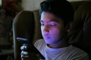 teenage boy sitting on sofa using smart phone at night photo
