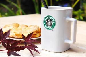 WASHINGTON, USA - August 01 2022  Coffee mug with Starbucks logo on front, white bakery on plate. Place it on a wooden table in the garden where the morning sun shines. photo