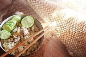 arroz frito con cerdo, arroz frito al estilo chino en un bol con pepino y limón servido en una mesa de madera marrón. foto