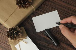 manos masculinas envolviendo regalos de año nuevo y escribiendo tarjetas en una mesa de madera marrón, vista superior, flatlay foto