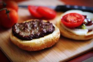 The hamburgers are being prepared on a wooden cutting board in the kitchen with fresh tomatoes. photo