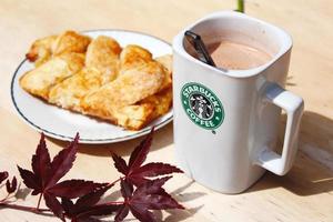 WASHINGTON, USA - August 01 2022  Coffee mug with Starbucks logo on front, white bakery on plate. Place it on a wooden table in the garden where the morning sun shines. photo