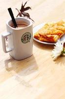 WASHINGTON, USA - August 01 2022  Coffee mug with Starbucks logo on front, white bakery on plate. Place it on a wooden table in the garden where the morning sun shines. photo