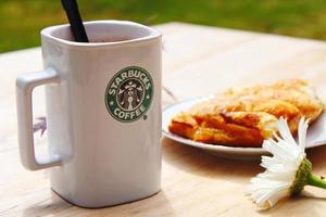 WASHINGTON, USA - August 01 2022  Coffee mug with Starbucks logo on front, white bakery on plate. Place it on a wooden table in the garden where the morning sun shines. photo