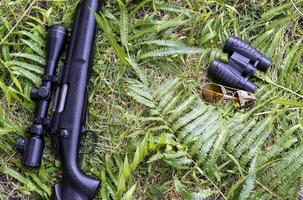 Top view rifle ,binoculars and sunglasses on grass floor photo