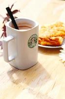 WASHINGTON, USA - August 01 2022  Coffee mug with Starbucks logo on front, white bakery on plate. Place it on a wooden table in the garden where the morning sun shines. photo