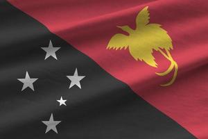 Papua New Guinea flag with big folds waving close up under the studio light indoors. The official symbols and colors in banner photo