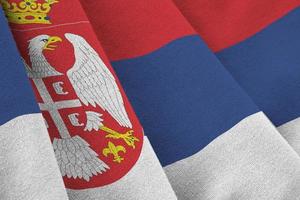 Serbia flag with big folds waving close up under the studio light indoors. The official symbols and colors in banner photo