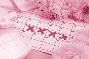 Menstrual pads and tampons on menstruation period calendar with white flowers on lilac background Image toned in Viva Magenta, color of the 2023 year photo